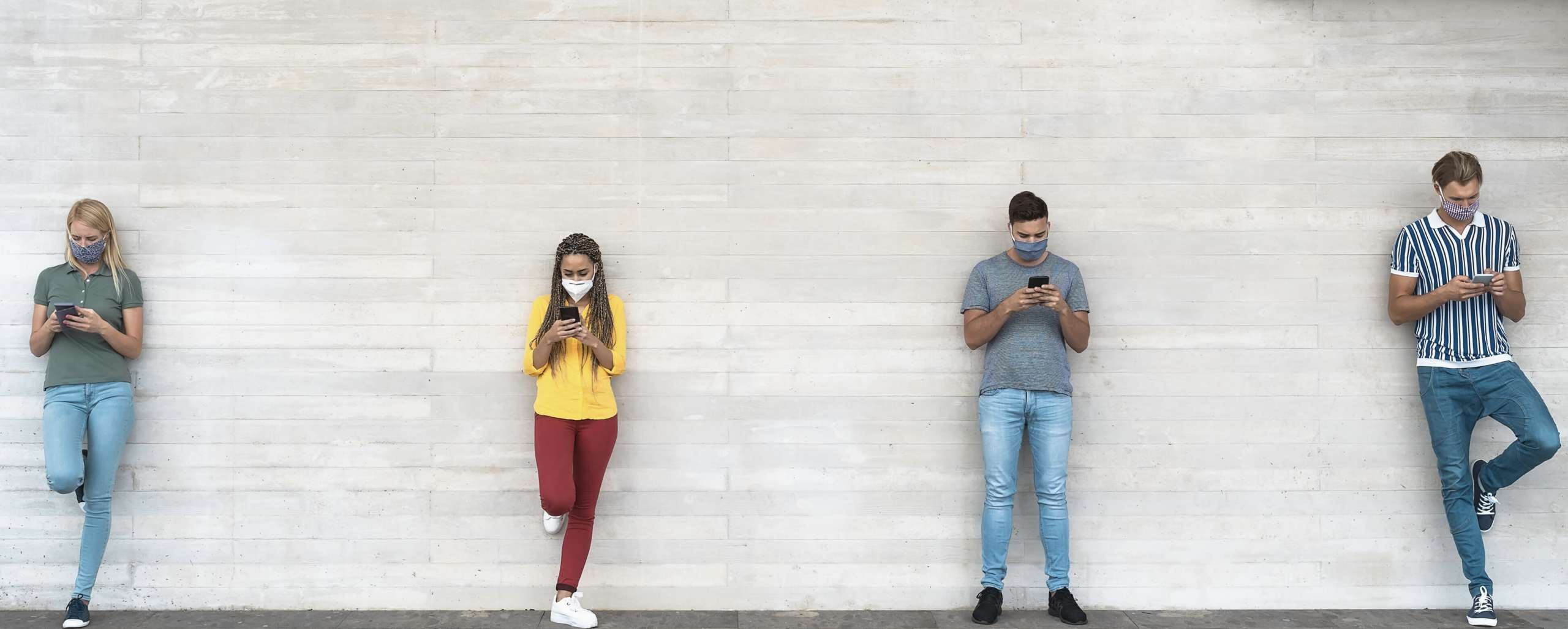 People standing six feet apart, looking at phones, and wearing masks